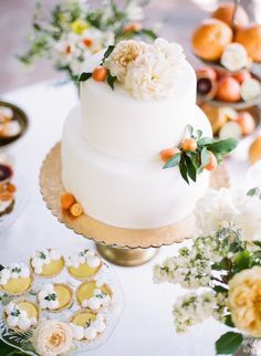 a three tiered white cake sitting on top of a table next to cupcakes