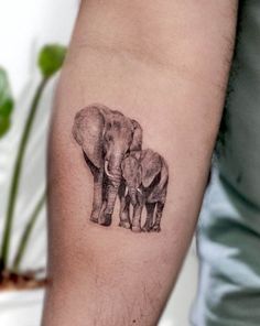 an elephant tattoo on the arm of a man's left arm, with two elephants standing next to each other