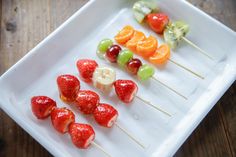 fruit skewers are arranged on a square white plate, ready to be eaten