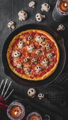 a pizza sitting on top of a pan covered in cheese and skulls next to candles