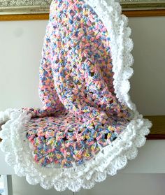 a crocheted blanket sitting on top of a white chair next to a painting