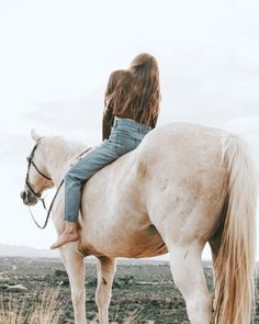 a woman riding on the back of a white horse in an open field with tall grass