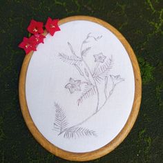 a close up of a embroidery on a wooden hoop with flowers in the middle and grass behind it