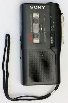 an old fashioned cassette player with a lanyard attached to it's side, sitting on a white surface