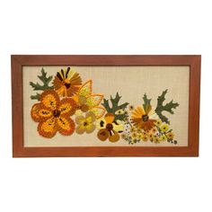 an embroidered wall hanging with flowers and leaves on the bottom, in a wooden frame