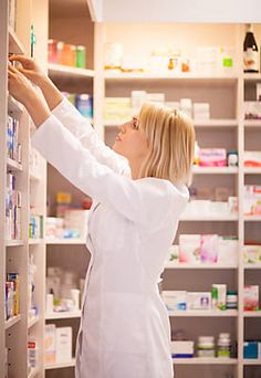 a woman in a white lab coat is looking at the shelves