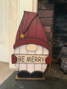 a wooden sign that says be merry with a gnome's hat on it sitting in front of a fireplace