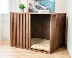 a wooden cabinet sitting on top of a hard wood floor next to a painting and a potted plant