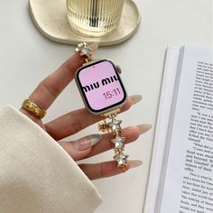 a woman's hand holding an apple watch with stars on it and a book in the background