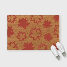 a pair of white shoes sitting on top of a brown rug with red maple leaves