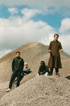 three people standing on top of a pile of rocks next to a man in a brown coat