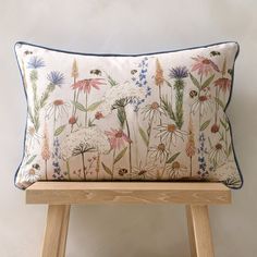 a pillow with flowers on it sitting on a wooden bench in front of a white wall