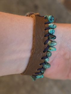 a person's arm with a bracelet made out of turquoise beads and brown leather