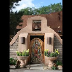 the entrance to an adobe style home with flowers and potted plants