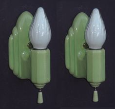 two green and white wall sconces on a black background, one has a light bulb attached to it