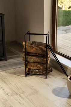 a stack of logs sitting on top of a wooden floor next to a vase and window