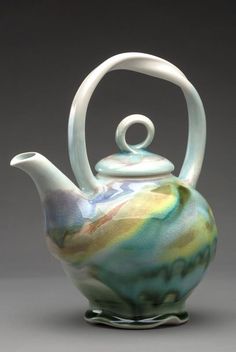 a glass teapot with a white handle and colorful swirls on the top, sitting on a gray surface