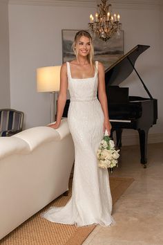 a woman in a wedding dress standing next to a grand piano and chandelier