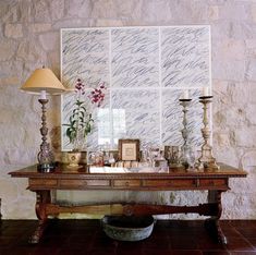 a wooden table topped with vases filled with flowers and candles next to a stone wall