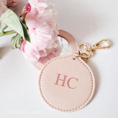 a pink keychain with a monogrammed h on it and flowers in the background