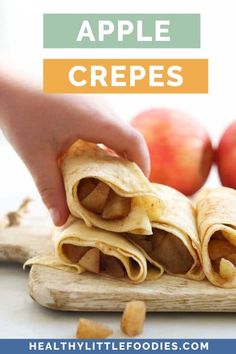 apple crepes cut in half and stacked on a cutting board with apples in the background