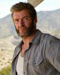 a man with a goatee and beard standing in front of a mountain range, looking at the camera