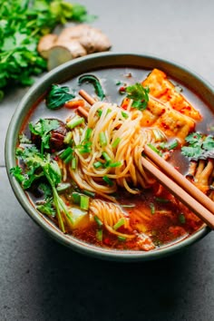 a bowl filled with noodles and vegetables next to chopsticks on a table top