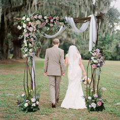 a bride and groom walking down the aisle under an arch decorated with pink, white and green flowers