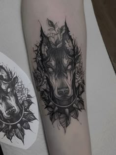 a black and white tattoo on the arm of a person with a wolf head surrounded by flowers