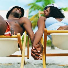 two people sitting in lawn chairs on the beach with one holding the other's hand