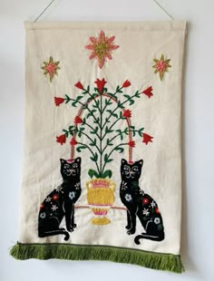 two black cats sitting next to each other on a white table cloth with red flowers