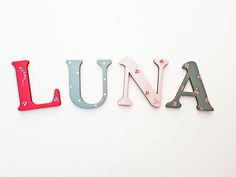 the word luna spelled with wooden letters on a white wall in front of a red and blue clock