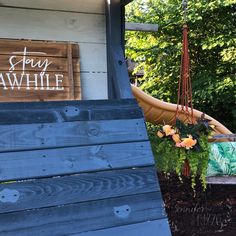 a wooden bench sitting in front of a sign on the side of a building with flowers hanging from it