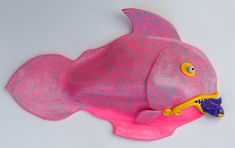 a pink plastic fish with yellow eyes on it's head and tail, sitting on a white surface