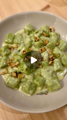 a white bowl filled with green food on top of a wooden table