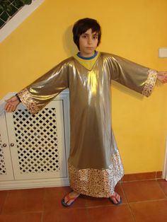 a young boy dressed in a silver outfit standing next to a yellow wall and holding his arms out