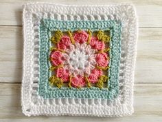 a crocheted square with pink and green flowers in the center on a wooden surface