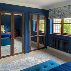 a bedroom with blue walls and carpeted flooring, two large mirrors on the wall