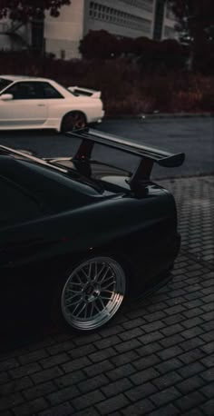 a black sports car is parked on the side of the road with another white car in the background