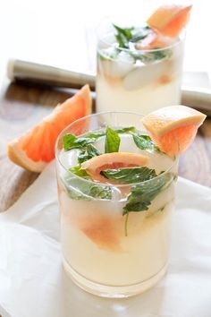 two glasses filled with watermelon, lime and mint garnish next to sliced oranges