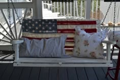 a porch swing with pillows on it and an american flag pillow hanging from the back