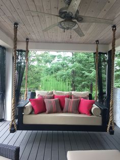 a porch swing with pillows on it and a ceiling fan hanging from the ceiling above