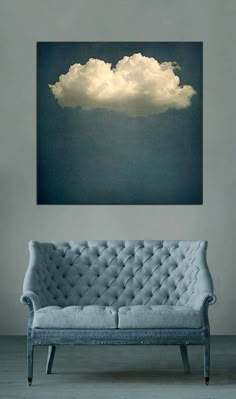 a couch sitting in front of a painting on the wall with clouds floating above it