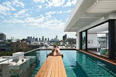 a woman sitting on the edge of a swimming pool in front of a cityscape