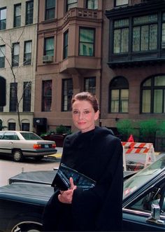 a woman standing in front of a black car on the street with her hand up