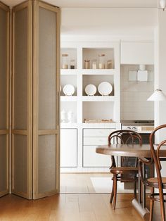 a dining room table and chairs in front of an open cabinet with white plates on it