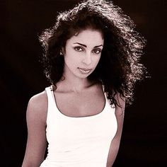 a black and white photo of a woman with long curly hair wearing a tank top