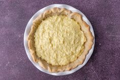 a pie sitting on top of a white plate next to a purple tablecloth and wall