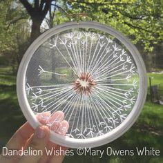 a person holding up a clear glass piece with white flowers on it in front of a tree