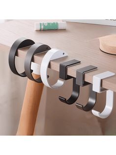 three metal hooks are attached to the side of a wooden table with a white and black handle